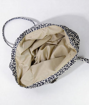 A top-down view of a soft-sided canvas tote bag with a black and white leopard print exterior and a beige interior lining, shown on a plain white background.