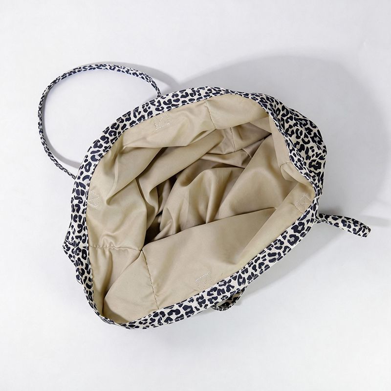 A top-down view of a soft-sided canvas tote bag with a black and white leopard print exterior and a beige interior lining, shown on a plain white background.
