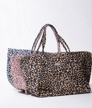 A large tote bag with a leopard print pattern in brown, beige, and black, featuring dual shoulder straps and a small white brand label on the front, displayed against a clean white background.