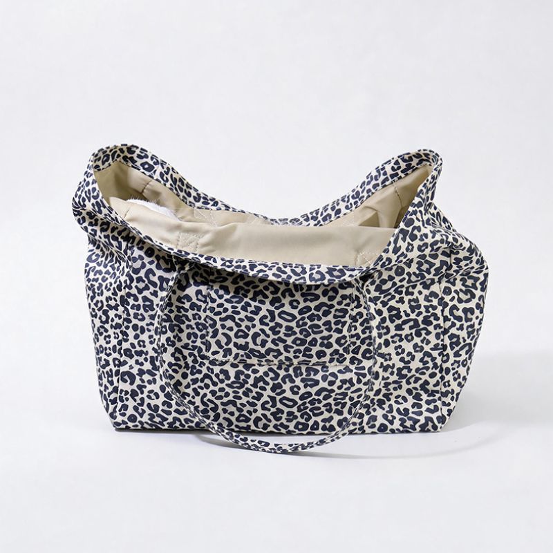 A soft fabric tote bag with a navy blue leopard print pattern on a cream background, featuring a beige interior lining and a matching shoulder strap, set against a plain white studio background.