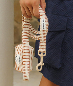 Striped dog leash with a small pouch held by a person wearing a blue textured outfit.