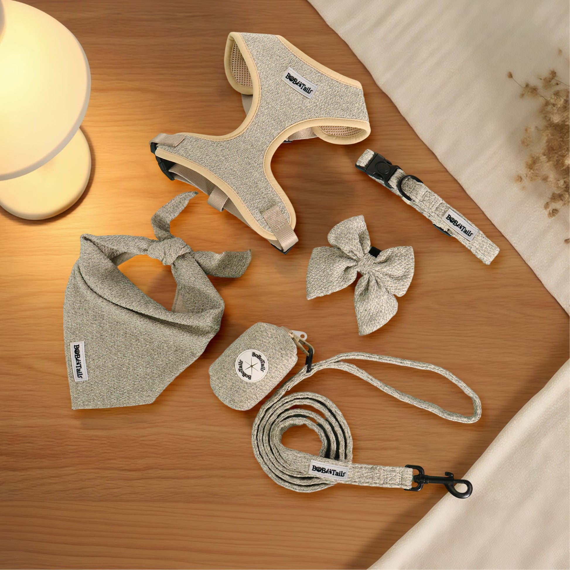 Dog accessories including a harness, leash, and collar ,bowtie,poop bag holder and bandana on a wooden surface.