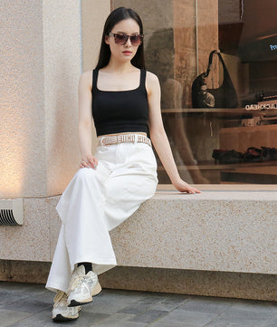 Woman in black top and white pants sitting on a ledge with a store window in the background